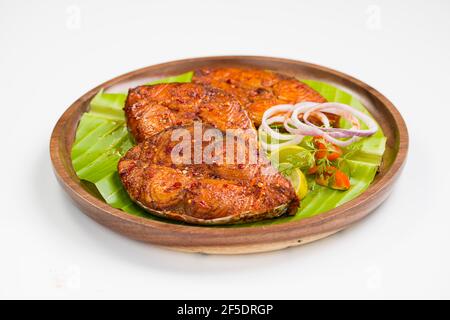 Seer fish fry arranged beautifully and garnished with onion, lemon and tomato slices on wooden plate lined with banana leaf. Stockfoto