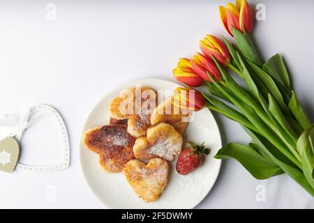 Herzen neben einem Teller mit herzförmigen Käsekuchen und Ein Bouquet von Tulpen Stockfoto