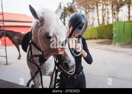 Junge kaukasische Frau, die ein weißes Pferd für einen Ritt vorbereitet Stockfoto