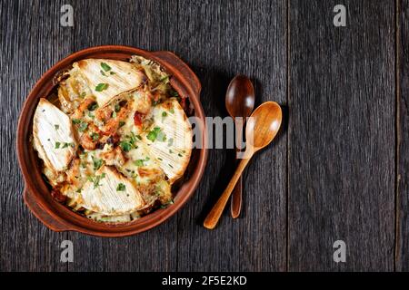 Tartiflette, French Potato, Bacon und Käse Auflauf in einer Tonschale auf einem dunklen Holztisch mit Löffel, flaches Lay, Freiraum, französische Küche Stockfoto