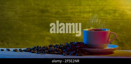 Bohnen mit Kaffeetasse auf dem Tisch. Dramatische Inneneinrichtung, die von farbigen Lichtern beleuchtet wird Stockfoto