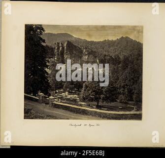 Kirchhof bei Nynee Tal. Blick auf den Friedhof in der Kirche St. John-in-the-Wilderness in Nainital. Der Friedhof liegt an einem Hang, oben von einer Steinmauer mit einem eisernen Tor auf der linken Seite begrenzt, das im Vordergrund entlang einer Feldstraße verläuft. Steinplatten und Grabsteine sind über den Friedhof Rasen sichtbar. Am Ende des Friedhofs liegt eine große Felswand, die teilweise mit Bäumen und anderer Vegetation bedeckt ist. (Recto, Montierung) unten links, handgeschrieben in Bleistift: 'A42,58 (Bou)' untere Mitte, handgeschrieben in schwarzer Tinte: 'Kirchhof bei Nynee Tâl' Stockfoto