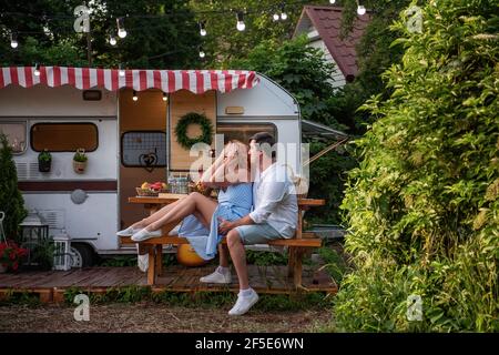 Ein junger Brünette küsst sanft ein schönes rothaariges Mädchen auf die Stirn, lacht sie. Nahaufnahme Porträt eines verliebten Paares, das sich auf einem Picknick ausruhte Stockfoto