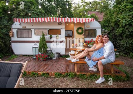 Ein junger Brünette küsst sanft ein schönes rothaariges Mädchen auf die Stirn, lacht sie. Nahaufnahme Porträt eines verliebten Paares, das sich auf einem Picknick ausruhte Stockfoto