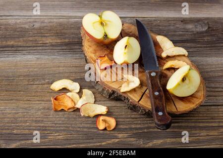 Ein Haufen getrockneter Apfelscheiben und frisch reife Äpfel auf Holzgrund. Getrocknete Fruchtchips. Gesundes veganes Essen Stockfoto