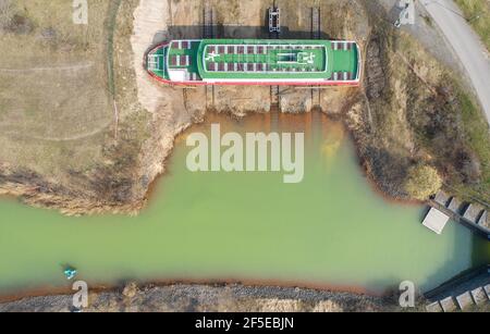 26. März 2021, Sachsen, Markkleeberg: Ein Ausflugsboot liegt trocken neben dem Störmthal-Kanal. Risse im Kanaldamm zwischen den Seen Markkleeberg und Störmthal erfordern sofortige Sicherheitsmaßnahmen. Der 850 Meter lange Störmthal-Kanal verbindet die beiden Seen - die betroffene Schleuse kompensiert die Differenz von vier Metern in den Wasserständen der beiden Gewässer. Experten zufolge würde ein vollständiger Einsturz zu großflächigen Überschwemmungen führen - in den nördlichen Stadtgebieten von Markkleeberg bis Leipzig. Jetzt sind Tauchen, Surfen, Segeln und Schwimmen sowie alle Bootstouren auf den Seen verboten Stockfoto