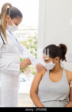 Patient, der einen Arzt aufsuchen muss, der einen Impfstoff auf den Arm anwendet. Weite Sicht. Vertikales Foto. Stockfoto