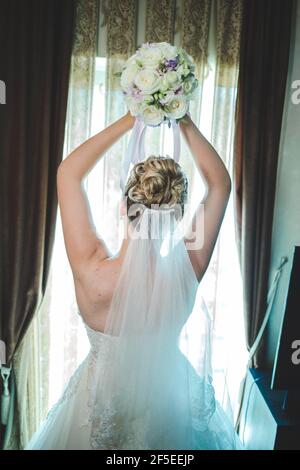 Vertikale Rückansicht einer Braut, die einen Strauß hält Ihr Kopf, bevor sie es werfen Stockfoto