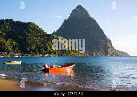 Soufriere, St. Lucia. Blick vom Sandstrand über die Soufriere Bay nach Petit Piton, abends, farbenprächtiges Fischerboot, das am Ufer festgemacht ist. Stockfoto