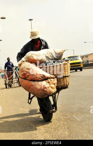 8. Lagos Metro: Ein Mann, der eine Schubkarre mit Tomaten auf dem Oshodi Market, Lagos, Nigeria, schiebt, um das tägliche Überleben zu sichern. Stockfoto