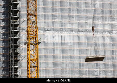 Essen, Nordrhein-Westfalen, Deutschland - Baukran hebt Betonteil vor die gerüstbemalte Bürofassade. Stockfoto