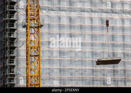 Essen, Nordrhein-Westfalen, Deutschland - Baukran hebt Betonteil vor die gerüstbemalte Bürofassade. Stockfoto