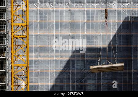 Essen, Nordrhein-Westfalen, Deutschland - Baukran hebt Betonteil vor die gerüstbemalte Bürofassade. Stockfoto