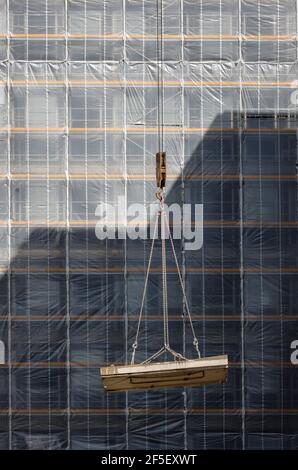 Essen, Nordrhein-Westfalen, Deutschland - Baukran hebt Betonteil vor die gerüstbemalte Bürofassade. Stockfoto