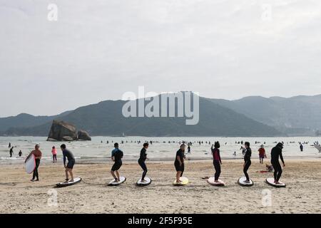 (210326) -- SANYA, 26. März 2021 (Xinhua) -- das Foto vom 25. Februar 2020 zeigt Touristen, die am Strand im Dorf Tenghai in Sanya, der südchinesischen Provinz Hainan, Surfkünste üben. Das Dorf Tenghai, einst ein kleines Fischerdorf, ist seit dem Surfboom in China ein berühmtes Surfcamp geworden, nachdem es offiziell für das Programm der Olympischen Spiele 2020 in Tokio zugelassen wurde. Das Dorf liegt in Sanya, der südchinesischen Provinz Hainan, und gewann auch Anerkennung für seine großartige Kombination aus Wassersport und Tourismusindustrie.Yang Xingfu, ein örtlicher Dorfbewohner, ist einer der frühesten Surfer in Tenghai. Yang Stockfoto