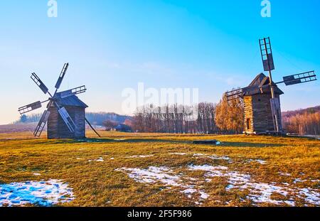 Erhaltene historische Windmühlen amif die breite schneebedeckte Wiese in Pyrohiv Skansen, Kiew, Ukraine Stockfoto