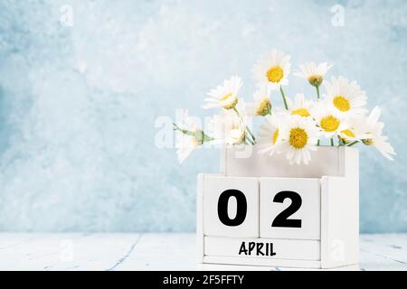 White Cube Kalender für april mit Gänseblümchen über geschmückt Blauer Hintergrund mit Kopierbereich Stockfoto