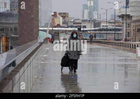 Eine Frau mit einer Gesichtsmaske geht allein über die London Bridge an einem kalten Wintermorgen im Westen Stockfoto