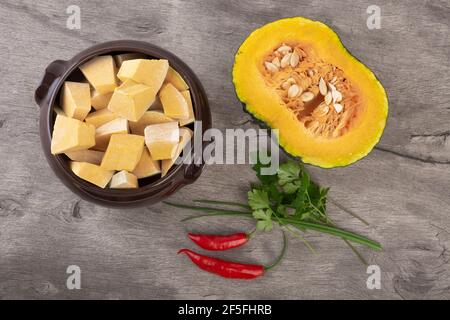 Draufsicht auf Kabocha-Stücke auf einer Schüssel mit halb Obst, Pfeffer und Kräutern. Stockfoto