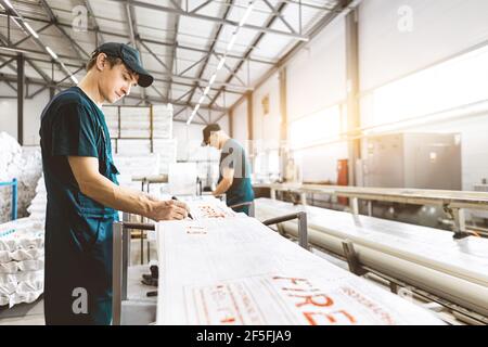 Die Arbeiter in der Fabrik erfüllen die technologischen Prozesse auf a Förderlinie in Schutzüberalls Stockfoto