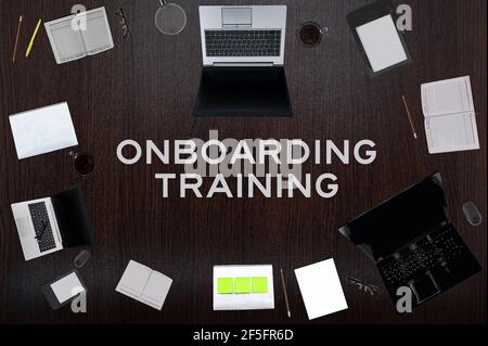 Draufsicht des Onboarding Trainingstextes auf dem Tisch mit Laptops, Notizblock, Kaffee, Brillen, Stiften. Geschäftskonzept. Stockfoto