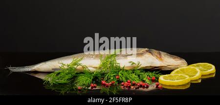 Der ganze Wolfsbarsch ist bereit zum Kochen mit Zitrone, Dill und rosa Pfefferkörnern Stockfoto