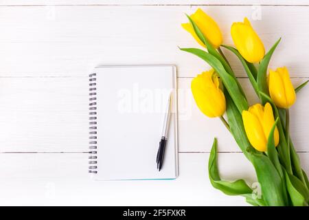 Schöne gelbe Tulpen und leeres Papier Notizbuch, Stift auf weißem Holzhintergrund. Stockfoto