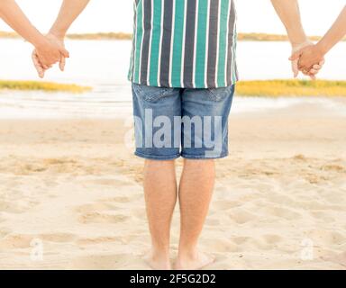 Junger Mann in Shorts und gestreiftem Hemd mit seinen Freunden am Strand. Freundschafts-, Reise- und Freizeitkonzept Stockfoto