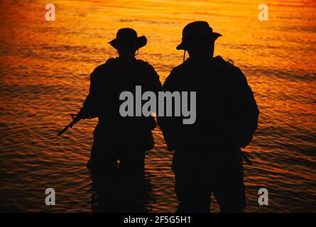 Zwei Kommandotruppen, Armee Spezialoperationsjäger zielen Sturmgewehre, während aus dem Wasser an der Küste bei Sonnenuntergang oder Morgendämmerung. Küstenwache Schützen landen an der Küste, schleichen sich im Wasser Stockfoto