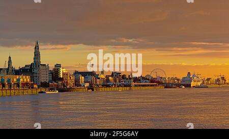 Kais des Flusses Schelde in Antwerpen, mit historischem Hafengebäude, Riesenrad, Wolkenkratzern und Kreuzfahrtschiff im trüben Abendlicht Stockfoto