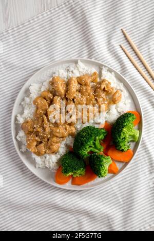 Hausgemachtes Orangenhuhn mit weißem Reis, Broccoli und Karotten auf einem Teller, Draufsicht. Flachlage, über Kopf, von oben. Stockfoto