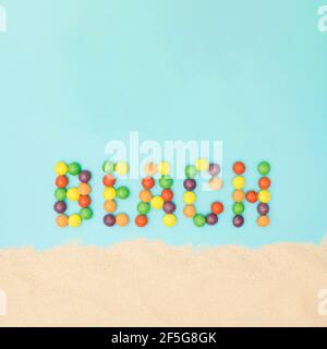 Strand Wort aus farbigen Kugeln auf einem blauen Hintergrund mit Sand gemacht. Tropischer Sommer Strand Konzept auf einem minimalen Hintergrund. Stockfoto