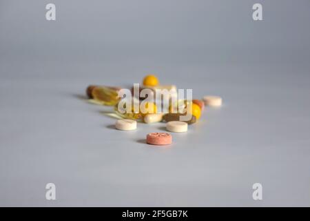 Tabletten, Kapseln, Vitamine und Nahrungsergänzungsmittel in verschiedenen Größen und Farben sind auf blauer Oberfläche verstreut. Konzentriere dich auf die orangefarbene Pille. Nahaufnahme. Stockfoto