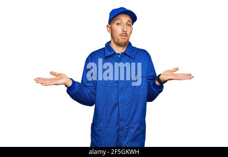 Glatze Mann mit Bart tragen Baumeister Jumpsuit Uniform ahnungslos und verwirrt Ausdruck mit Armen und Händen angehoben. Zweifel Konzept. Stockfoto