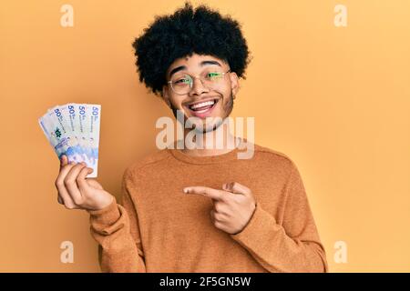 Junger afroamerikanischer Mann mit Afro-Haar hält 50 Mexikaner Pesos Banknoten lächelnd glücklich zeigen mit Hand und Finger Stockfoto