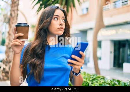 Junge hispanic Frau mit serios Ausdruck mit Smartphone und trinken Take Away Kaffee in der Stadt. Stockfoto