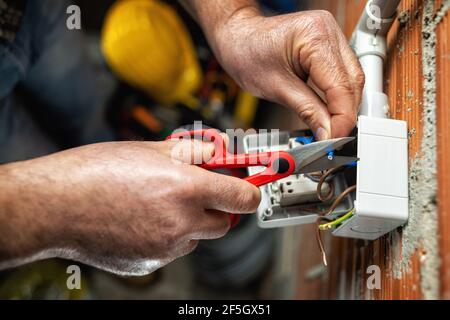 Blick von oben. Der Elektriker Arbeiter bei der Arbeit mit der Schere bereitet die elektrischen Kabel des häuslichen elektrischen Systems vor. Bauindustrie. Stockfoto