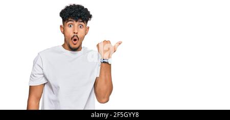 Junger arabischer Mann trägt casual weißes T-Shirt überrascht zeigt mit dem Finger auf die Seite, offenen Mund erstaunt Ausdruck. Stockfoto