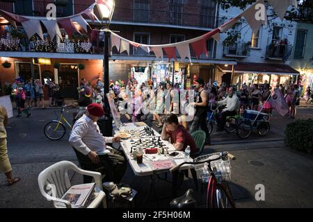 Schachmeister Jude Acers spielt ein Spiel auf der Decatur Street im French Quarter, während eine Parade vorbeizieht und den lebendigen Geist von New Orleans fängt. Stockfoto