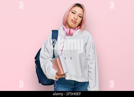 Hispanische Frau mit rosa Haaren tragen Student Rucksack und Kopfhörer suchen schläfrig und müde, erschöpft für Müdigkeit und Kater, faule Augen in der m Stockfoto