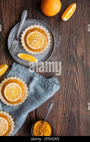 Kurkuma-Törtchen aus Vollweizen, gefüllt mit Aprikosenmarmelade, verziert mit getrockneten Orangen, gekrönt mit Puderzucker auf rustikalem Holzhintergrund Stockfoto