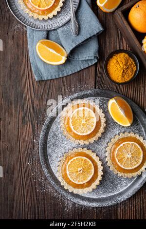 Kurkuma-Törtchen aus Vollweizen, gefüllt mit Aprikosenmarmelade, verziert mit getrockneten Orangen, gekrönt mit Puderzucker auf rustikalem Holzhintergrund Stockfoto