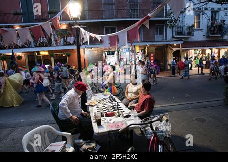 Schachmeister Jude Acers spielt ein Spiel auf der Decatur Street im French Quarter, während eine Parade vorbeizieht und den lebendigen Geist von New Orleans fängt. Stockfoto