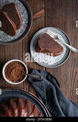 Köstliches Dessert, dunkle Schokolade gebündelt Kuchen gekrönt mit Ganache Glasur auf rustikalem Holzhintergrund Stockfoto