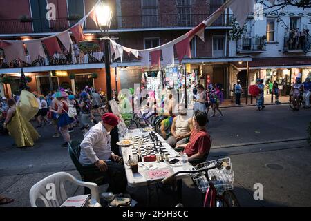 Schachmeister Jude Acers spielt ein Spiel auf der Decatur Street im French Quarter, während eine Parade vorbeizieht und den lebendigen Geist von New Orleans fängt. Stockfoto