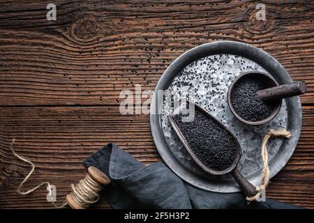 Nigella sativa Samen auch bekannt als schwarzer Kreuzkümmel, Kalo jeera, Kalonji und schwarzer Kümmel in Eisenkelle und Mörtel auf rustikalem Holzhintergrund mit Kopie s Stockfoto