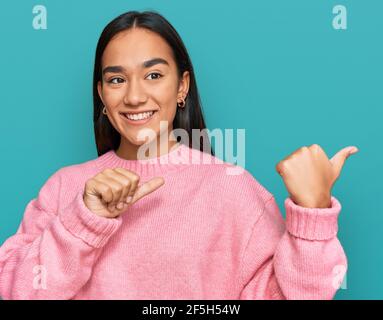 Junge asiatische Frau trägt lässige Winter Pullover zeigt auf den Rücken hinter mit Hand und Daumen nach oben, lächelnd zuversichtlich Stockfoto