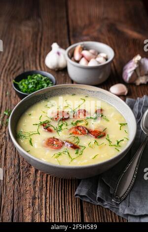 Caldo Verde Suppe aus wirsing-Kohl, pürierten Kartoffeln, Zwiebeln, Knoblauch und gebratenen Wurstscheiben in einer Keramikschale auf rustikalem Holzhintergrund Stockfoto