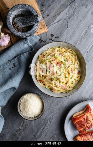 Klassische Pasta Carbonara in einer Keramikplatte, herzhaftes italienisches Gericht mit Spaghetti, Ei, gebratenem Speck, gekrönt mit geriebenem Parmesan-Käse und schwarzem pe Stockfoto