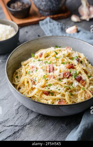 Klassische Pasta Carbonara in einer Keramikplatte, herzhaftes italienisches Gericht mit Spaghetti, Ei, gebratenem Speck, gekrönt mit geriebenem Parmesan-Käse und schwarzem pe Stockfoto